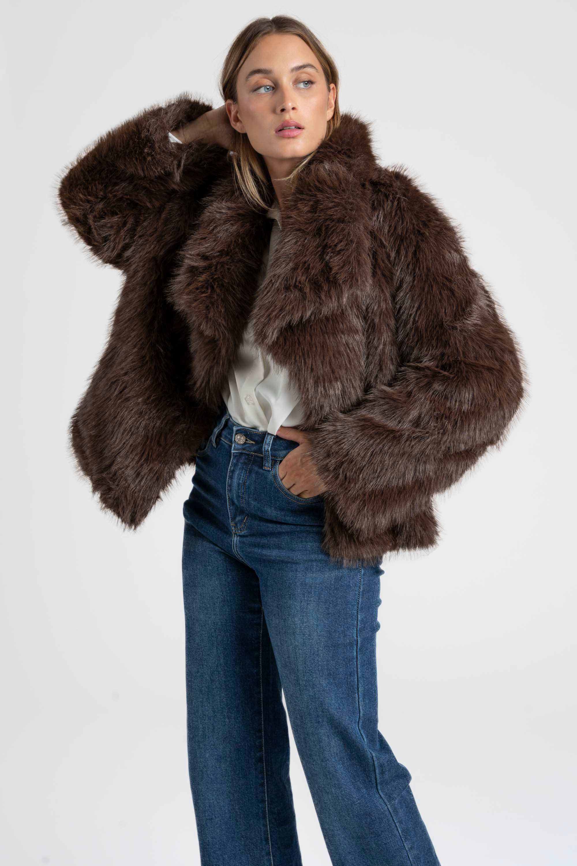 Femme avec une Veste fausse fourrure marron, style oversize, associée à un pantalon en denim pour une allure moderne.