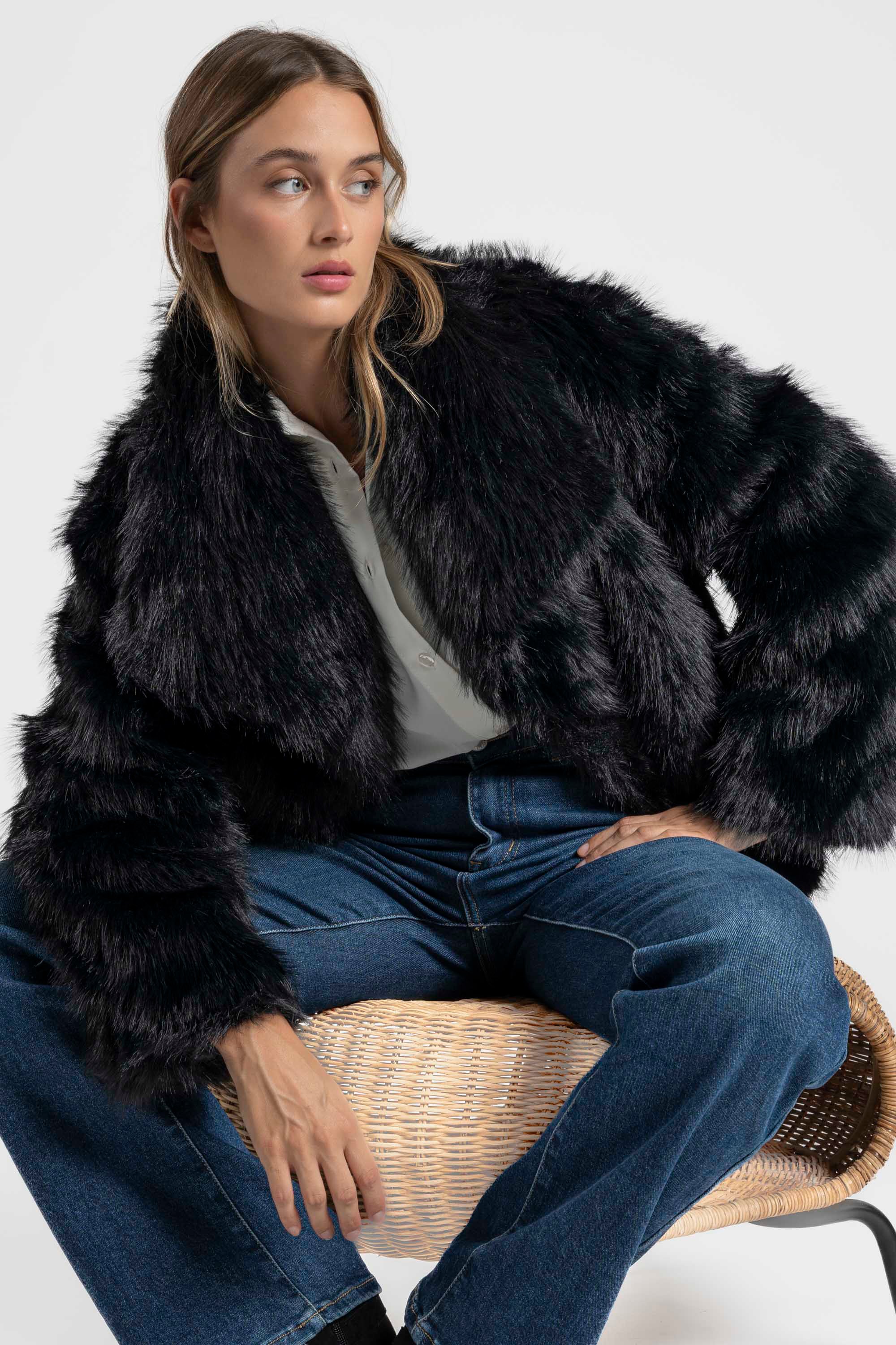 Femme au style moderne, en Veste fausse fourrure noire, posant avec assurance dans un cadre urbain.