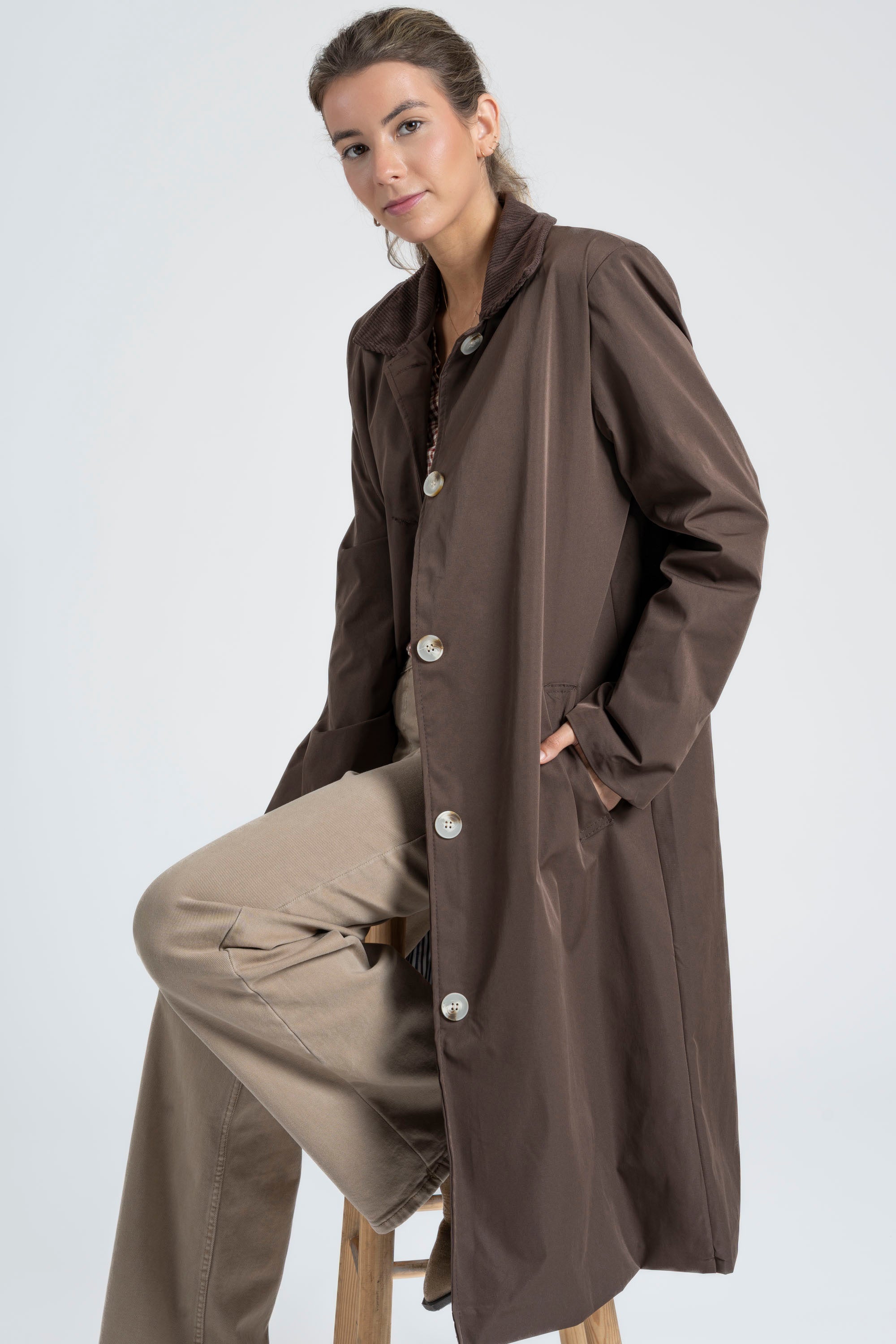 Profile d'une femme avec une Veste imperméable Coupe droite Col velours assise sur une chaise en bois.