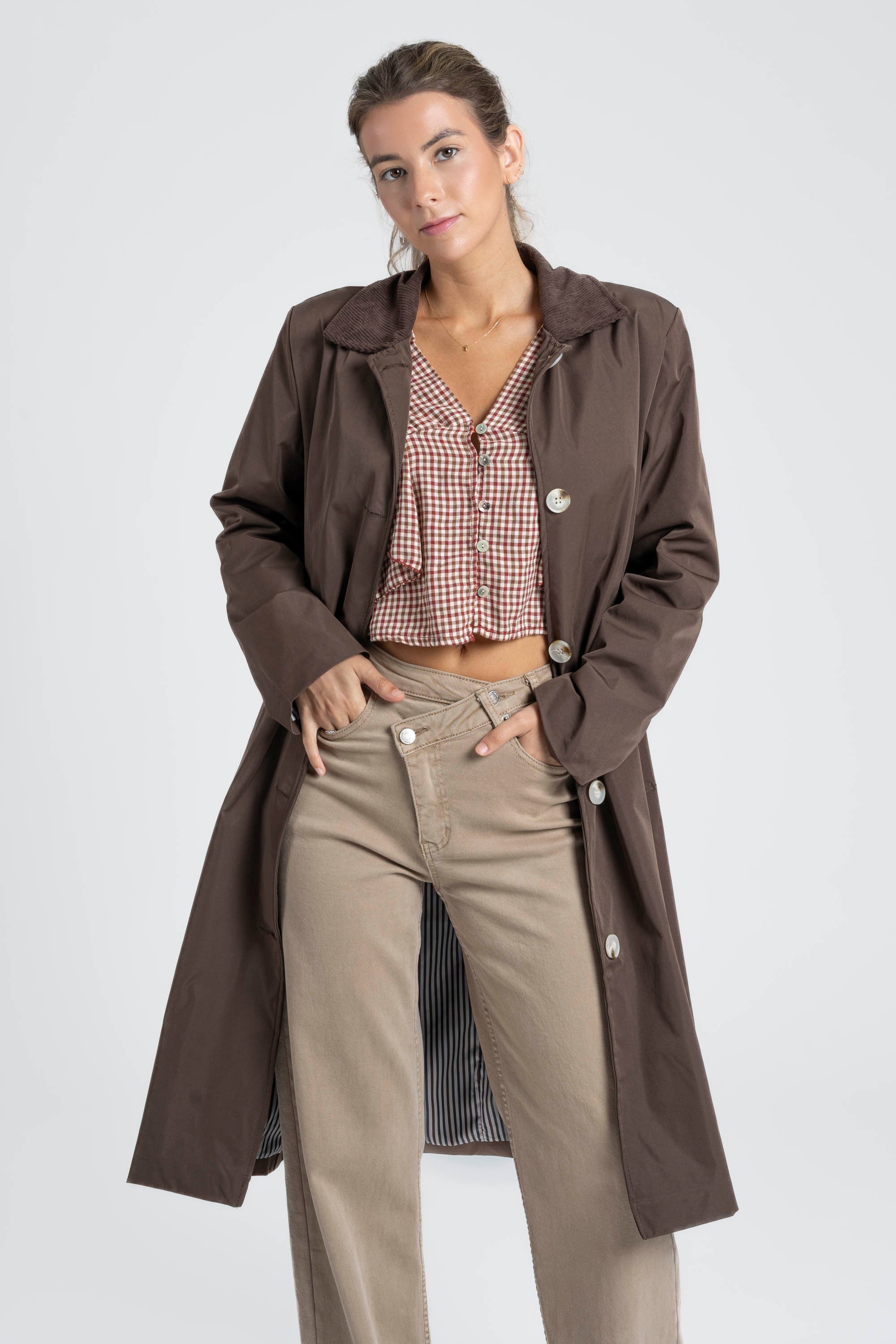 Femme souriante en Veste imperméable Coupe droite Col velours, associée à un haut à carreaux et des pantalons beiges.