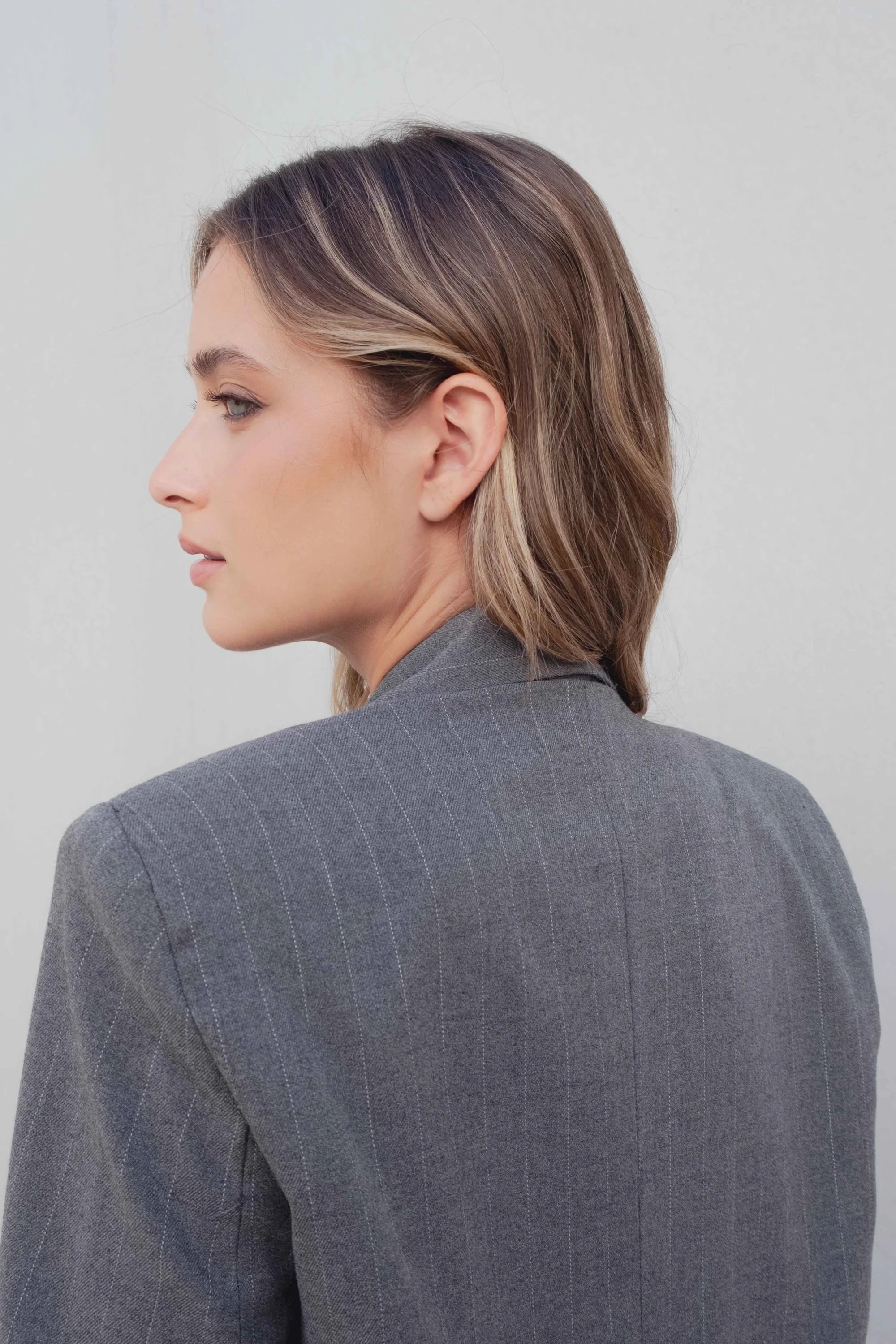 Profil d'une femme portant un blazer femme chic gris à rayures fines, mettant en évidence le design contemporain et stylé.