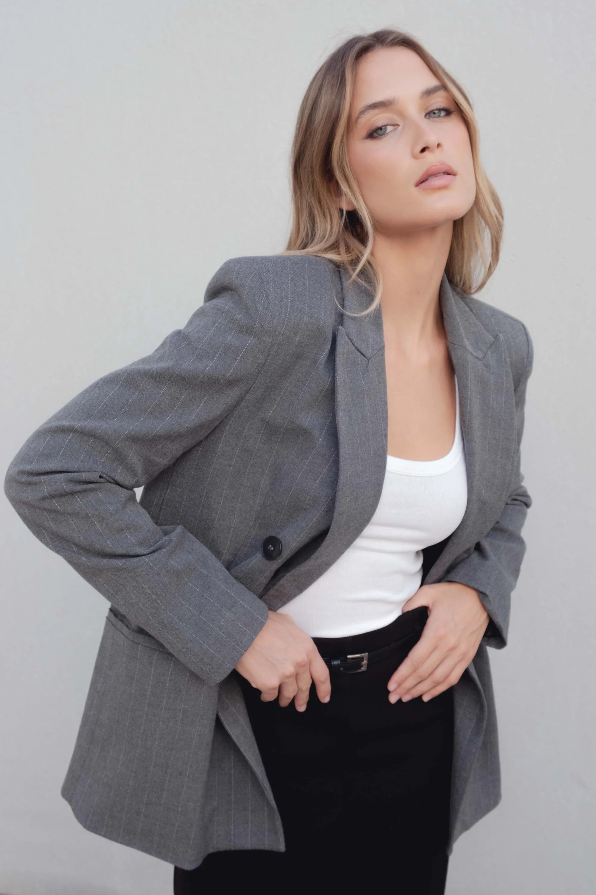 Détail du blazer femme chic gris à rayures fines, mettant en avant la coupe et le tissu fluide sur un fond neutre.