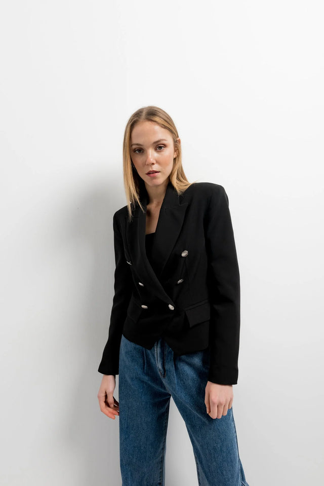 Femme portant une veste blazer noir femme boutonnée à double poitrine, associée à un pantalon décontracté, idéale pour un look moderne et élégant.