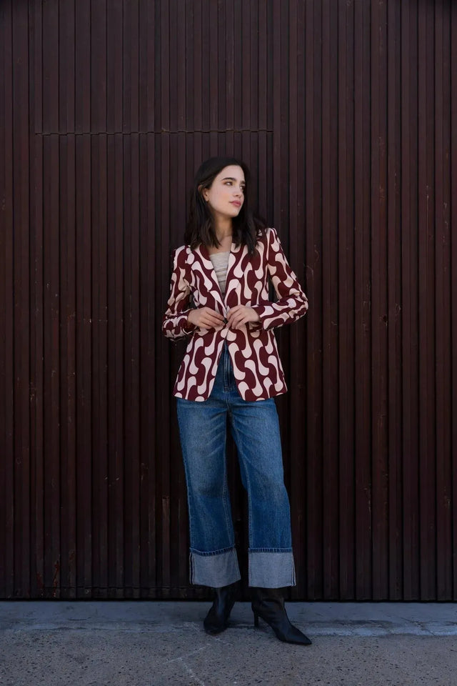 Vue profil d'une femme en blazer imprimé tendance femme chic avec un motif contemporain, associée à un haut beige et un jean, soulignant le style unique du blazer motif femme.