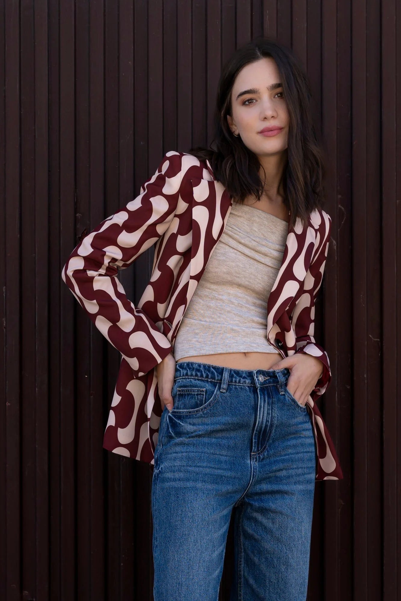 Femme portant un blazer imprimé tendance femme chic, avec un motif graphique audacieux, associé à un haut beige et un jean, mettant en avant le style du blazer motif femme.