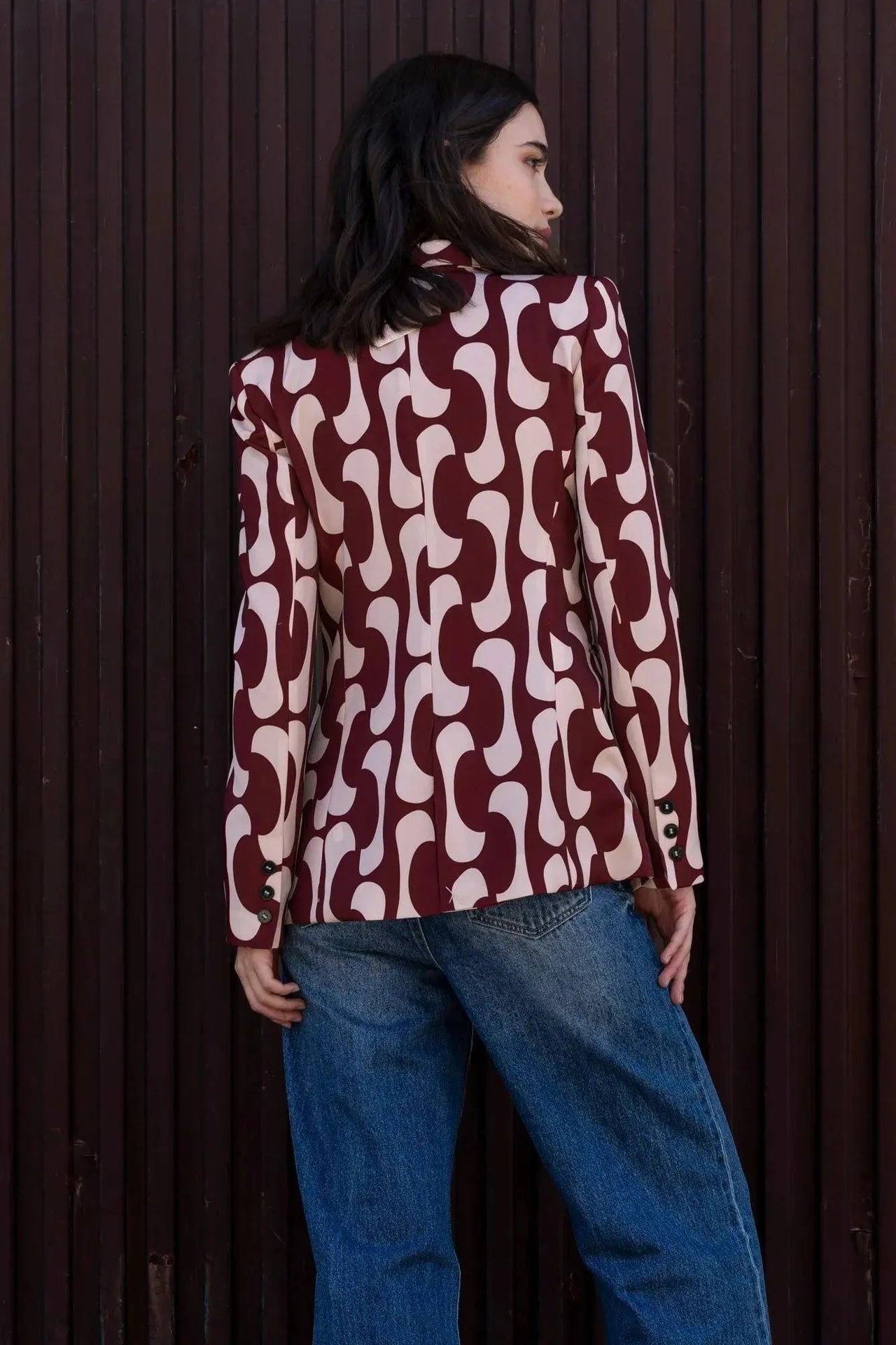Femme montrant le dos de son blazer imprimé tendance femme chic avec un motif graphique, coordonné avec un jean, mettant en lumière la coupe élégante du blazer motif femme.