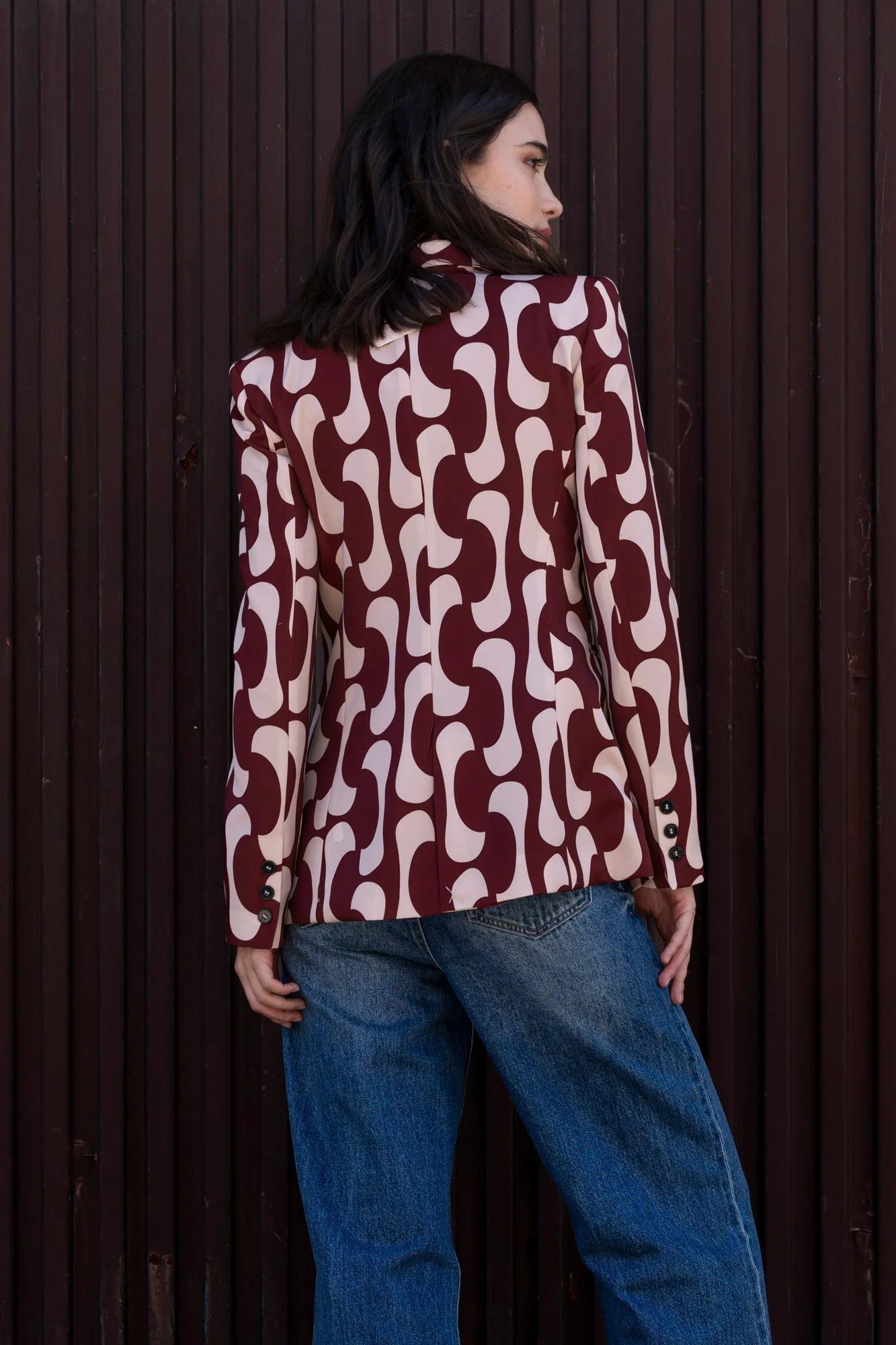 Femme montrant le dos de son blazer imprimé tendance femme chic avec un motif graphique, coordonné avec un jean, mettant en lumière la coupe élégante du blazer motif femme.