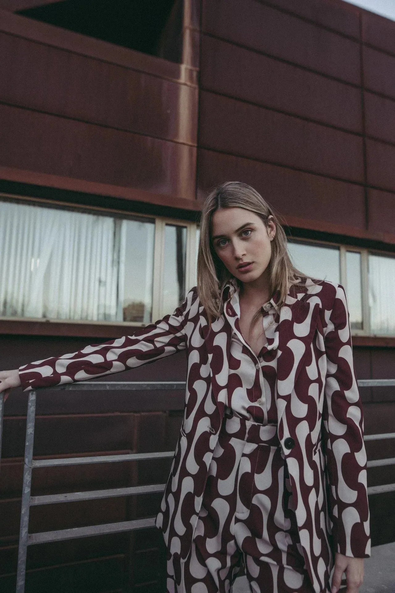Femme dans un blazer imprimé tendance femme chic, se tenant parmi des palmiers, affichant un style décontracté et original du blazer motif femme.