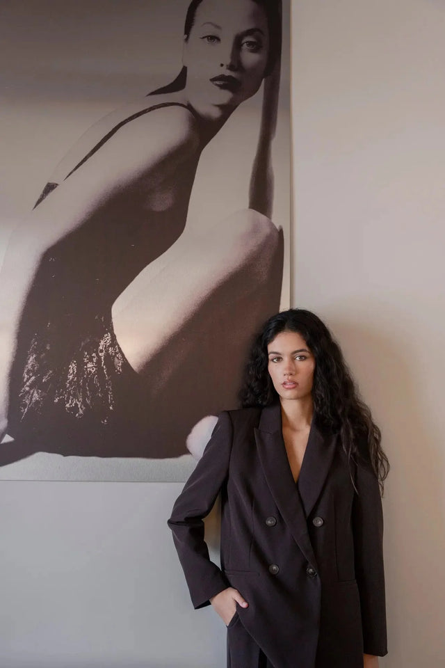 Femme portant un blazer double boutonnage femme oversize chic et confortable, posant devant un mur avec une œuvre d'art. Idéal pour un look élégant.