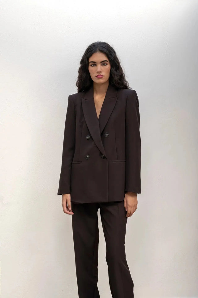 Femme dans un blazer double boutonnage femme, pose simple contre un mur, mettant l'accent sur le confort et le style sophistiqué.