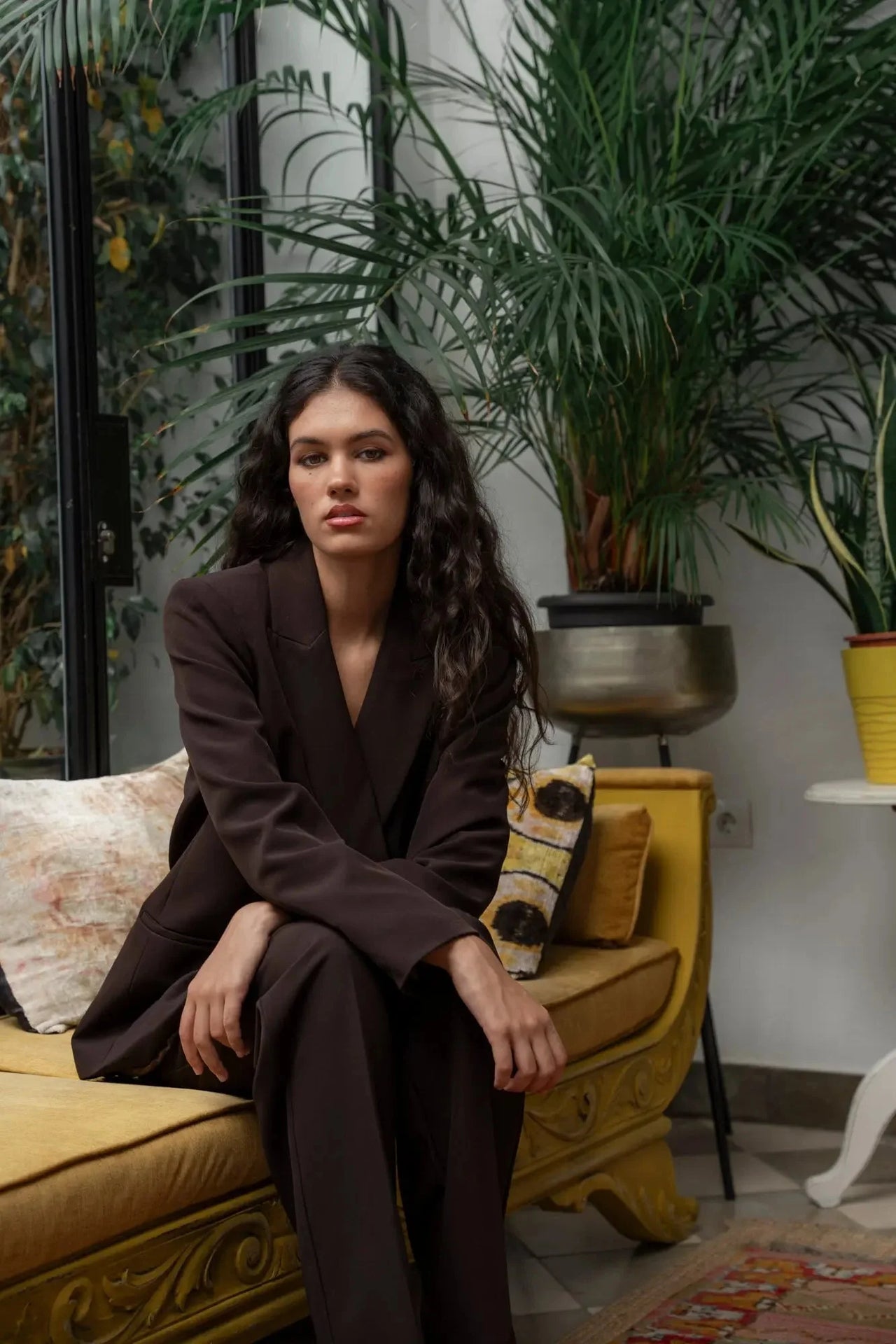 Femme avec un blazer double boutonnage femme, assise dans un cadre confortable avec des plantes, soulignant le style chic et décontracté.