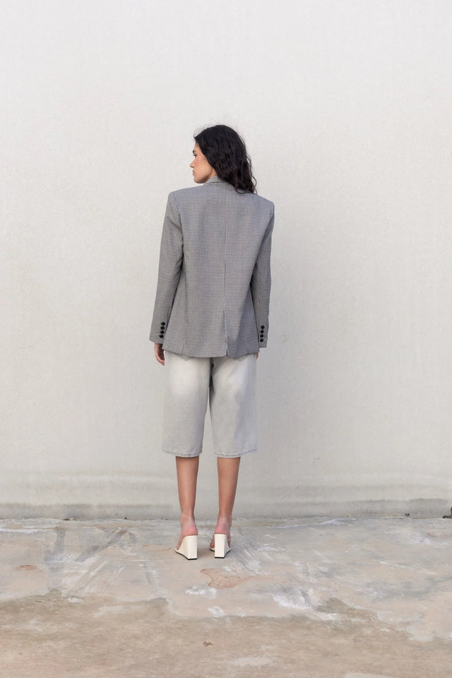 Femme portant un blazer pied-de-poule gris, bermudas en denim clair et mules blanches