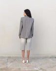 Femme portant un blazer pied-de-poule gris, bermudas en denim clair et mules blanches