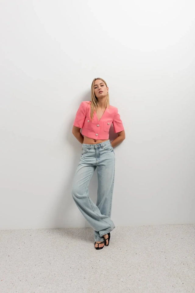 Femme debout avec un blazer recadré rose à manches courtes, look décontracté et élégant, mettant en valeur un blazer crop top.