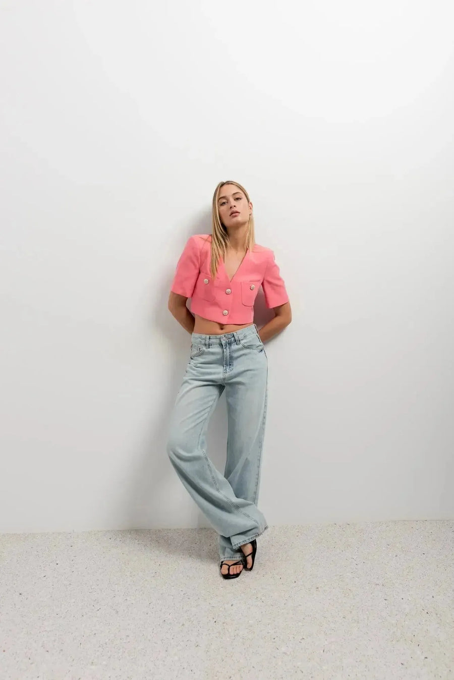 Femme debout avec un blazer recadré rose à manches courtes, look décontracté et élégant, mettant en valeur un blazer crop top.
