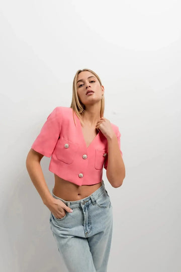 Femme portant un blazer recadré rose à manches courtes, associé à un haut décontracté, style chic et moderne, blazer crop top.