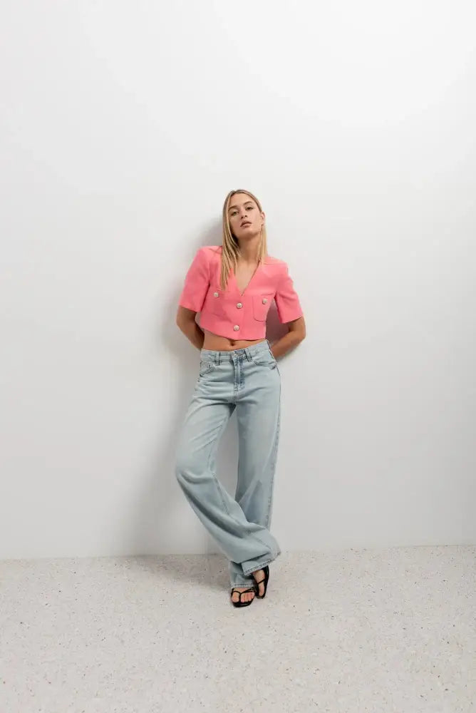 Femme portant un blazer recadré rose à manches courtes avec crop top rose et jeans décontractés