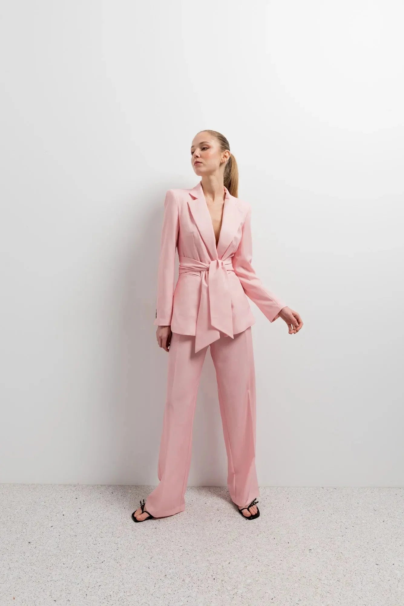 Femme posant avec style dans un Blazer Rose Femme Ceinturé, accompagné de pantalon assorti pour un look harmonieux.