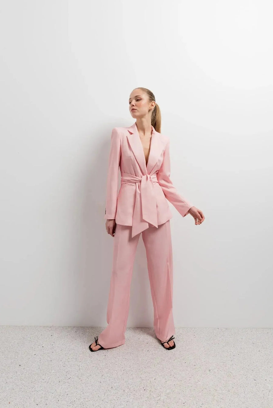 Femme posant avec style dans un Blazer Rose Femme Ceinturé, accompagné de pantalon assorti pour un look harmonieux.