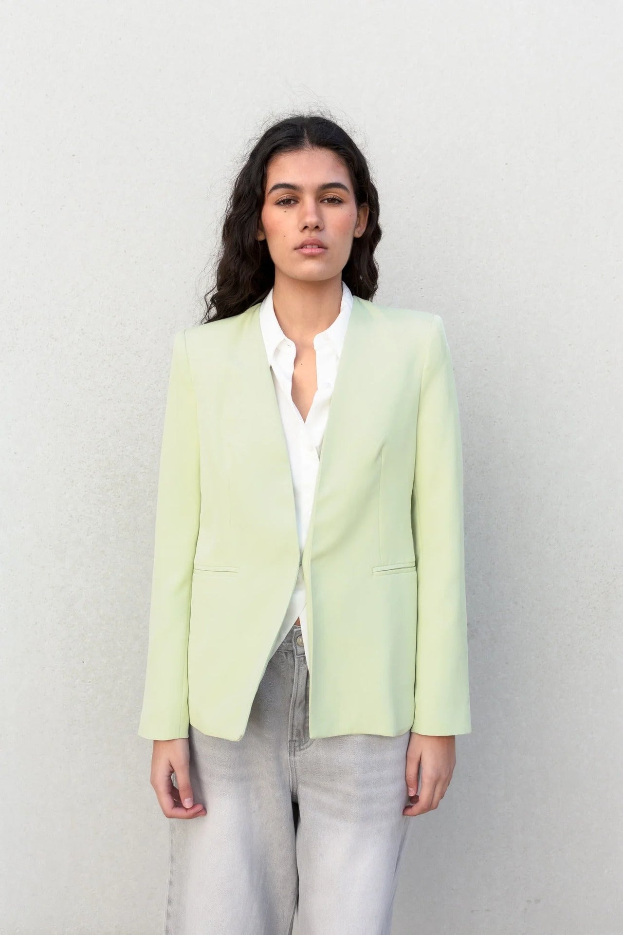 Portrait d'une femme avec une veste vert pastel femme sans col, stylée avec une chemise blanche pour un look chic.
