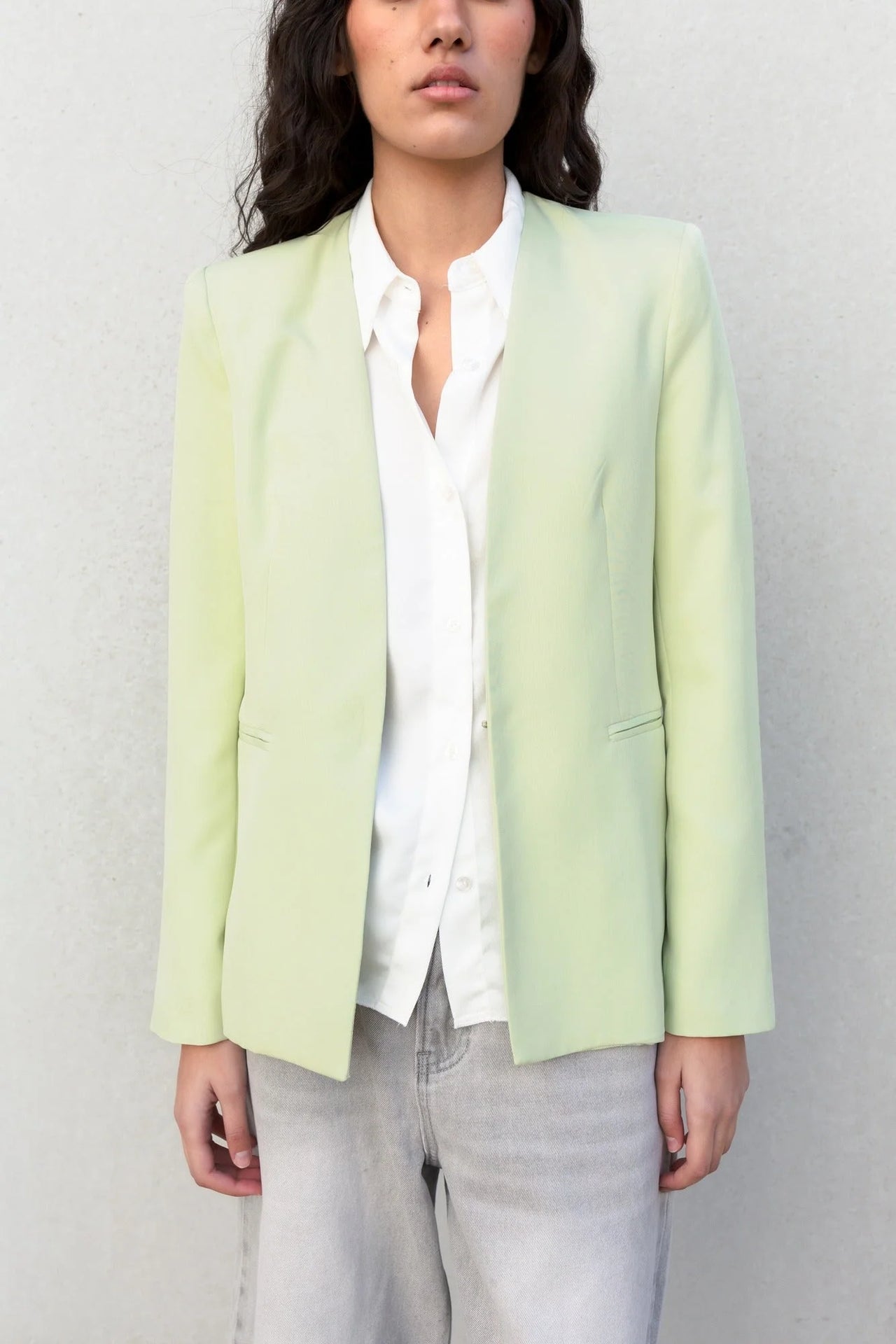 Modèle portant une veste vert pastel femme sans col avec une chemise blanche, parfaite pour une tenue élégante et moderne.