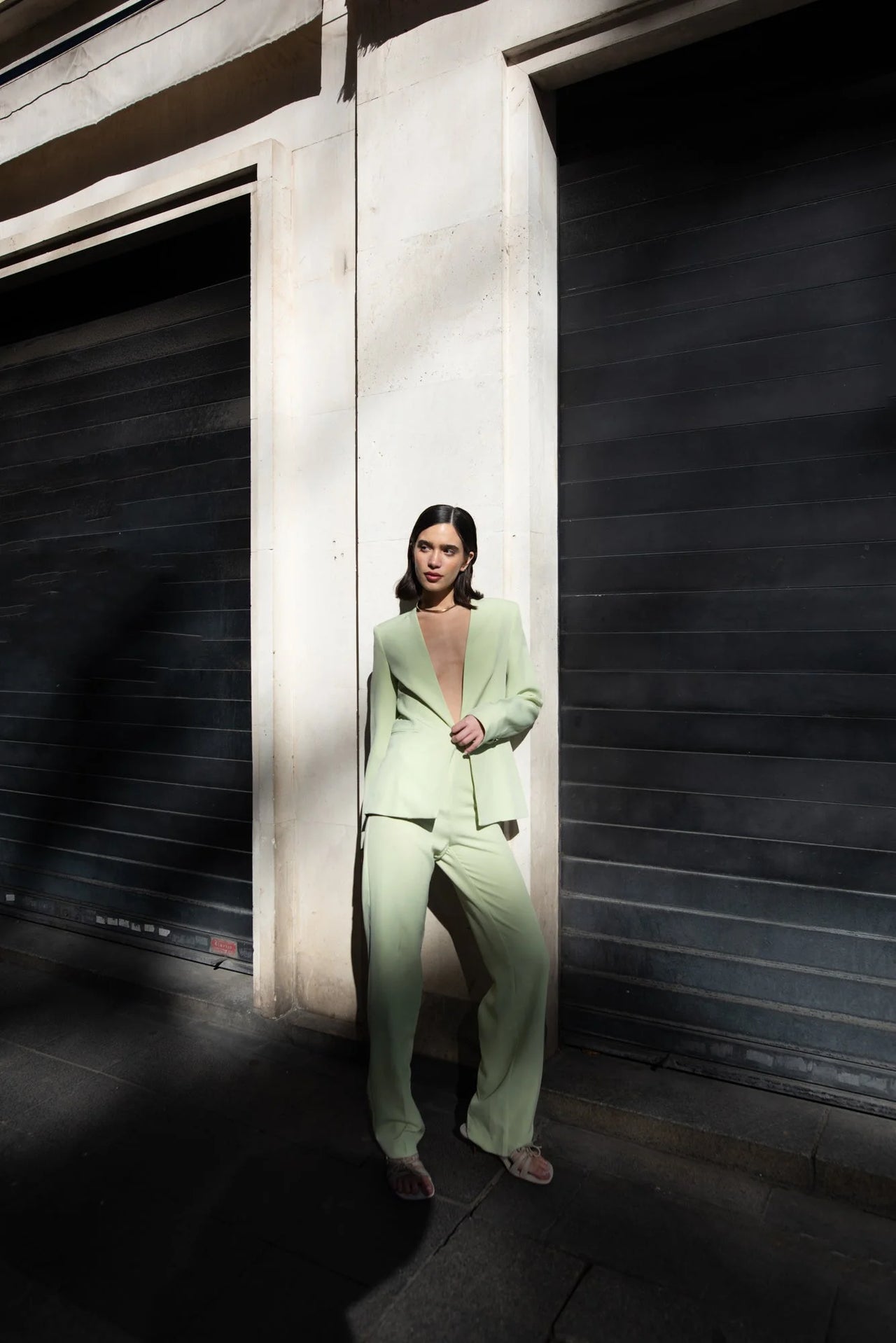 Modèle posant en extérieur avec une veste vert pastel femme sans col, associée à un ensemble décontracté, capturant un style urbain.