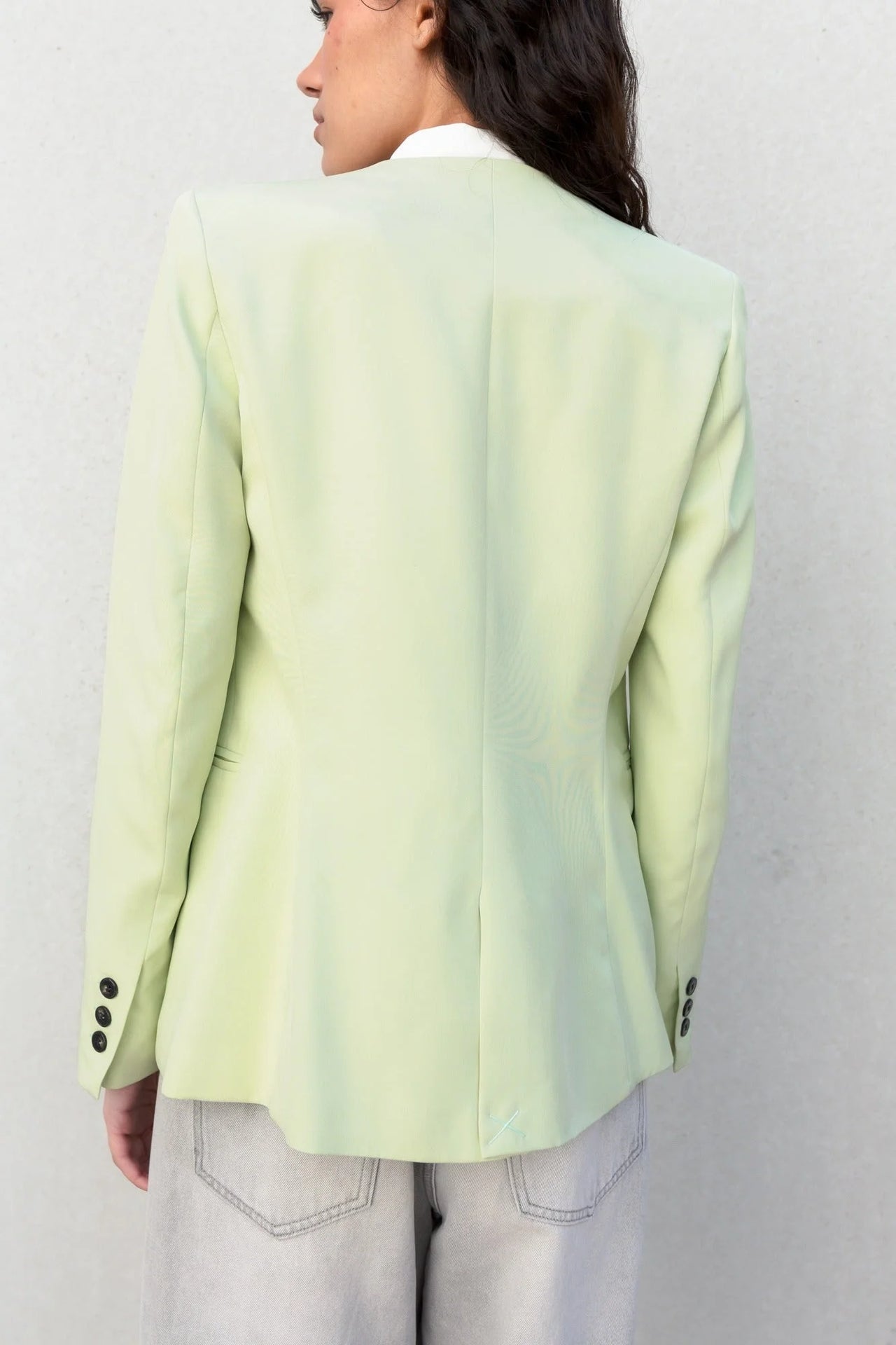Détails de l'arrière d'une veste vert pastel femme sans col, montrant la coupe élégante et moderne.
