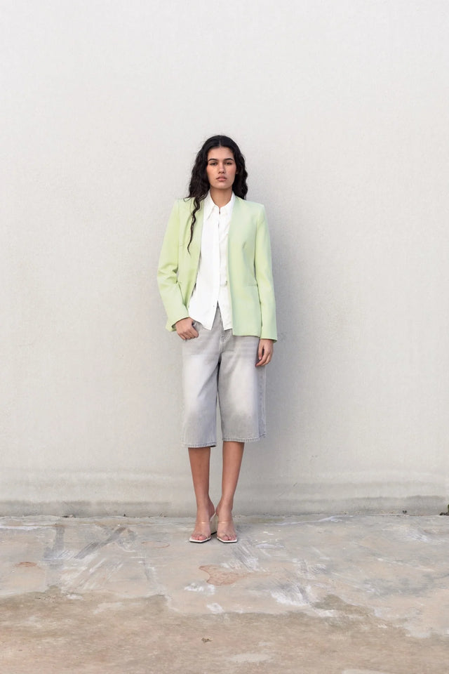 Femme debout avec une veste vert pastel femme sans col et un pantalon en jean, un style versatile convenant à diverses occasions.