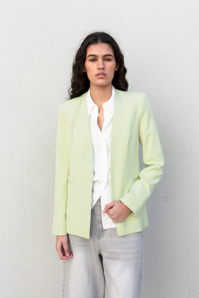 Vue frontale d'une veste vert pastel femme sans col, mise en valeur avec une chemise blanche pour un style chic et décontracté.