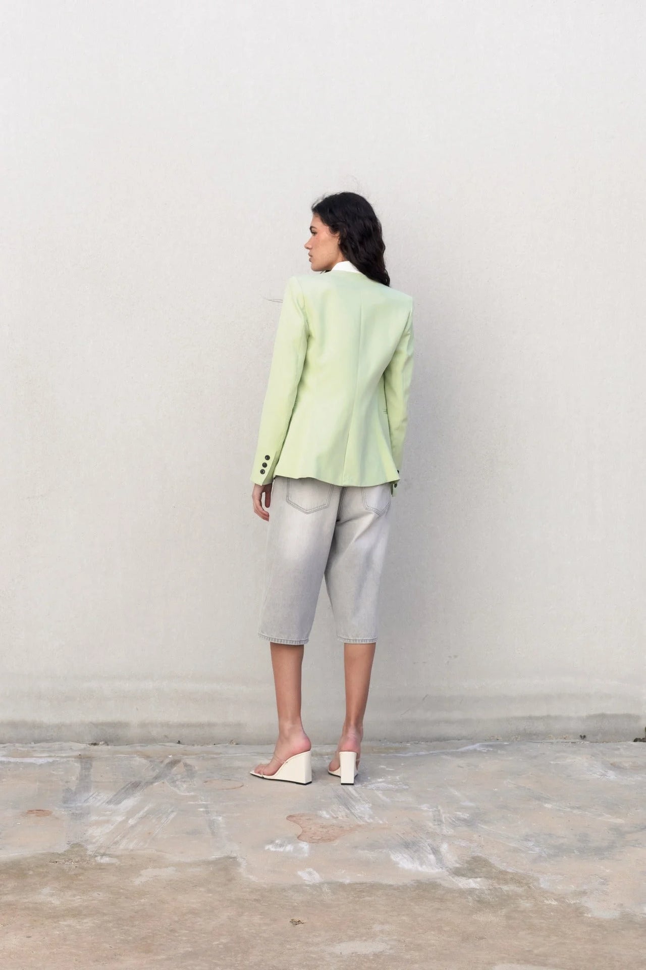 Femme vue de dos portant une veste vert pastel sans col, associée à un pantalon court pour un look tendance.