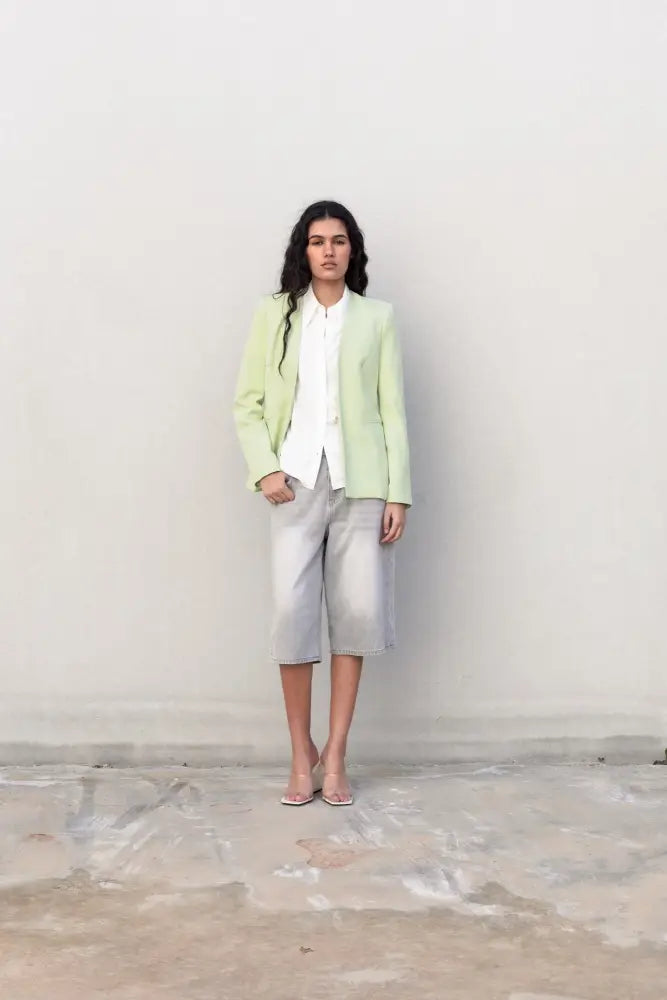Femme en blazer sans rabat vert clair, chemise blanche, shorts gris, talons transparents