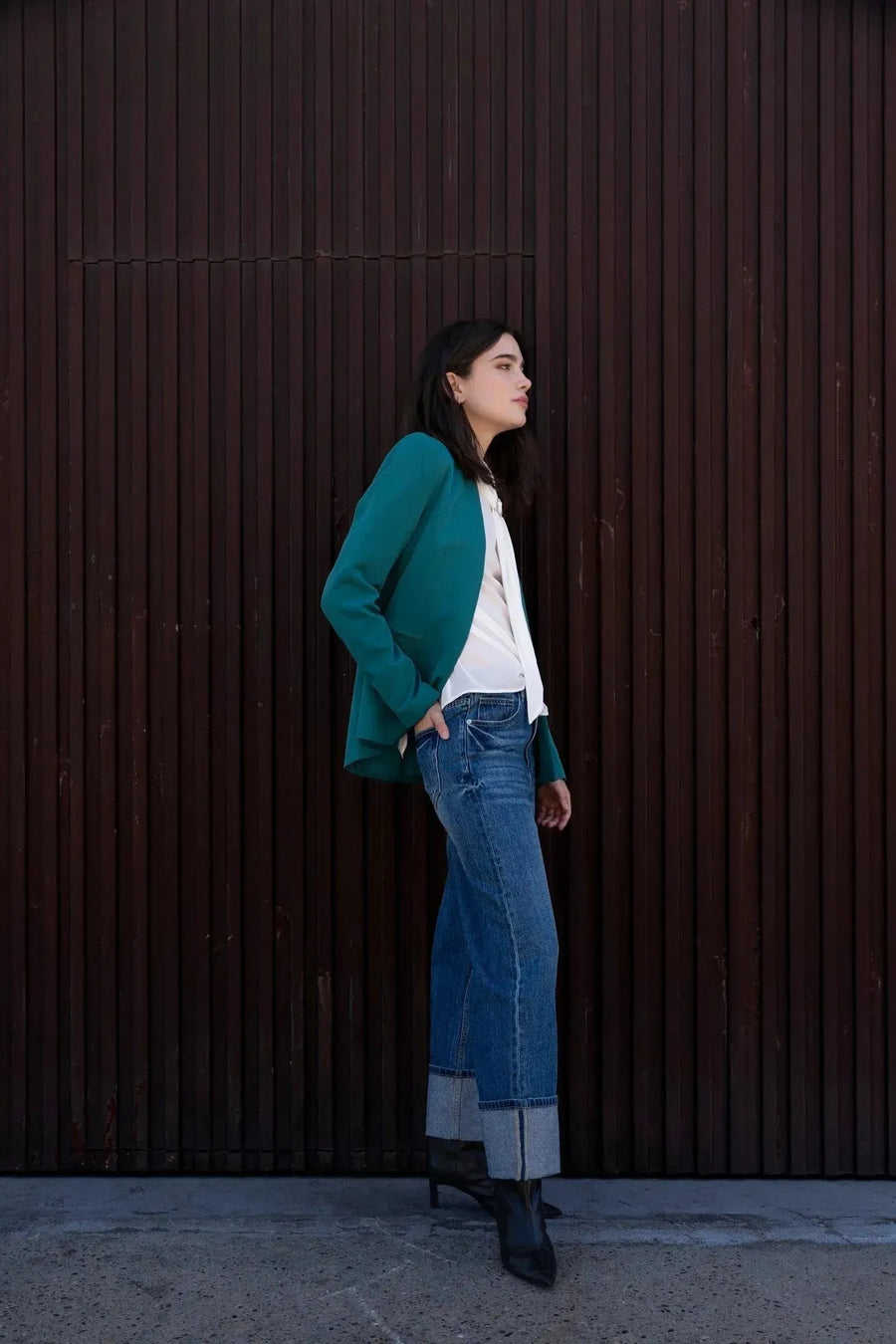 Profil d'une femme en blazer vert femme, ajusté sans col, se tenant de manière décontractée, avec un jean tendance pour un look élégant et moderne.