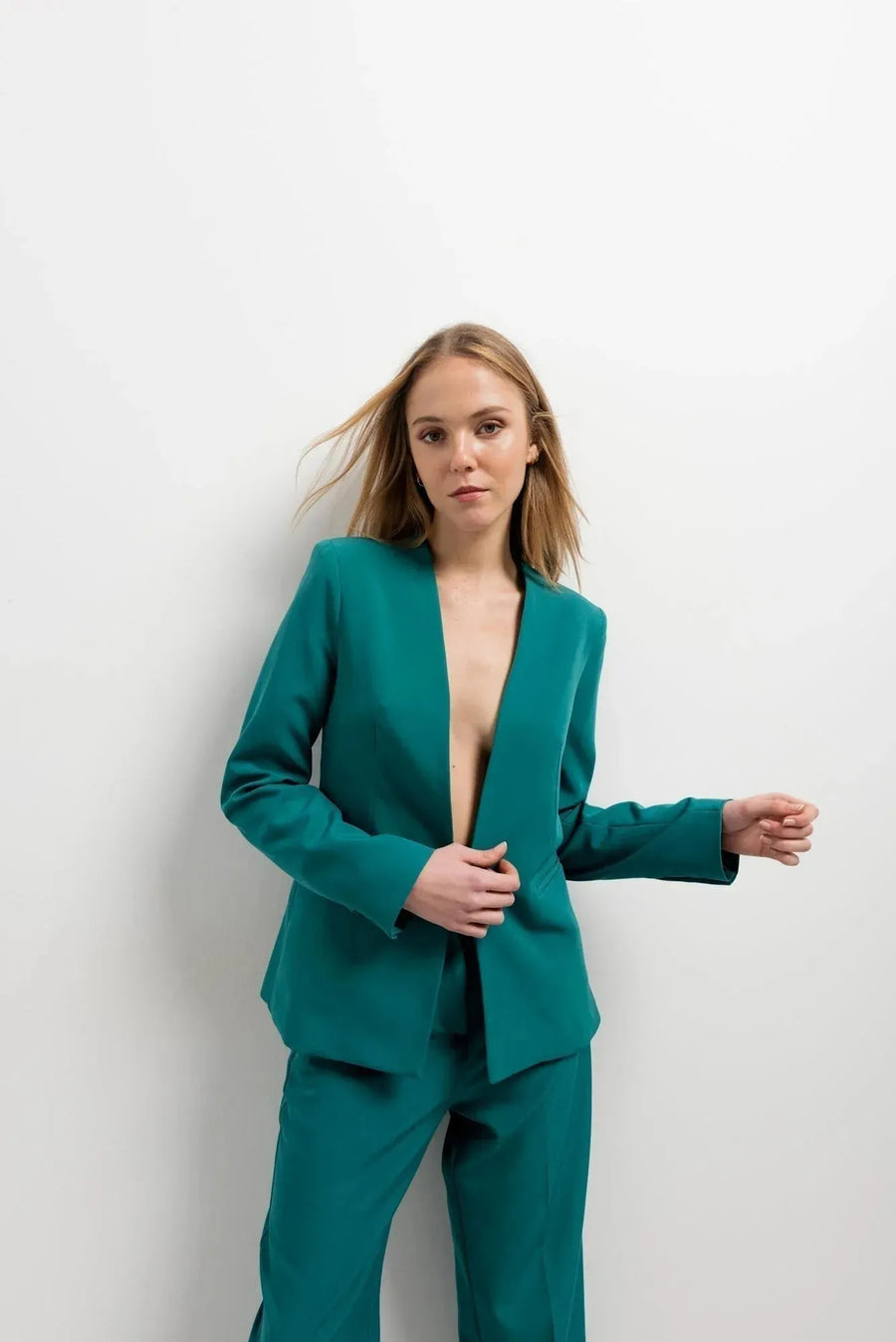 Femme posant en blazer vert femme sans col, offrant une allure chic, associée à un design minimaliste et un pantalon coordonné pour un look stylé.