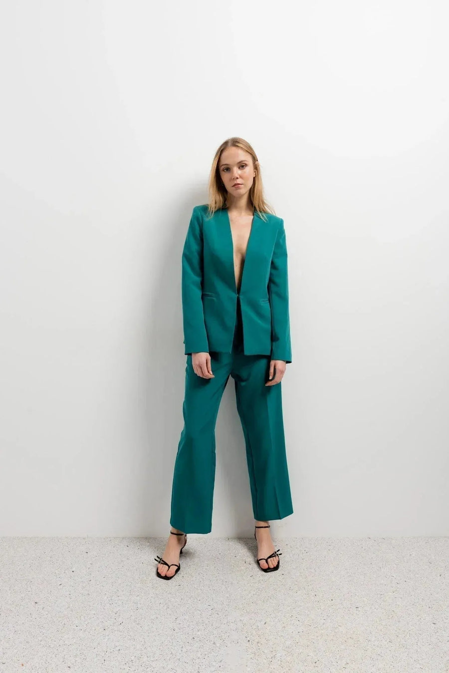 Femme élégante en blazer vert femme sans col et pantalon assorti, se tenant debout, illustrant le style haut de gamme et contemporain parfait pour diverses occasions.