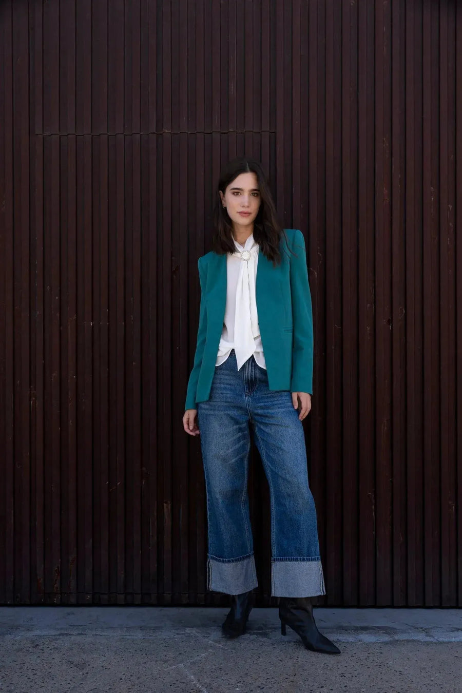 Femme portant un blazer vert ajusté sans col, parfait pour toutes les occasions, associé à une blouse blanche et un jean décontracté. Idéal pour un style chic et contemporain.