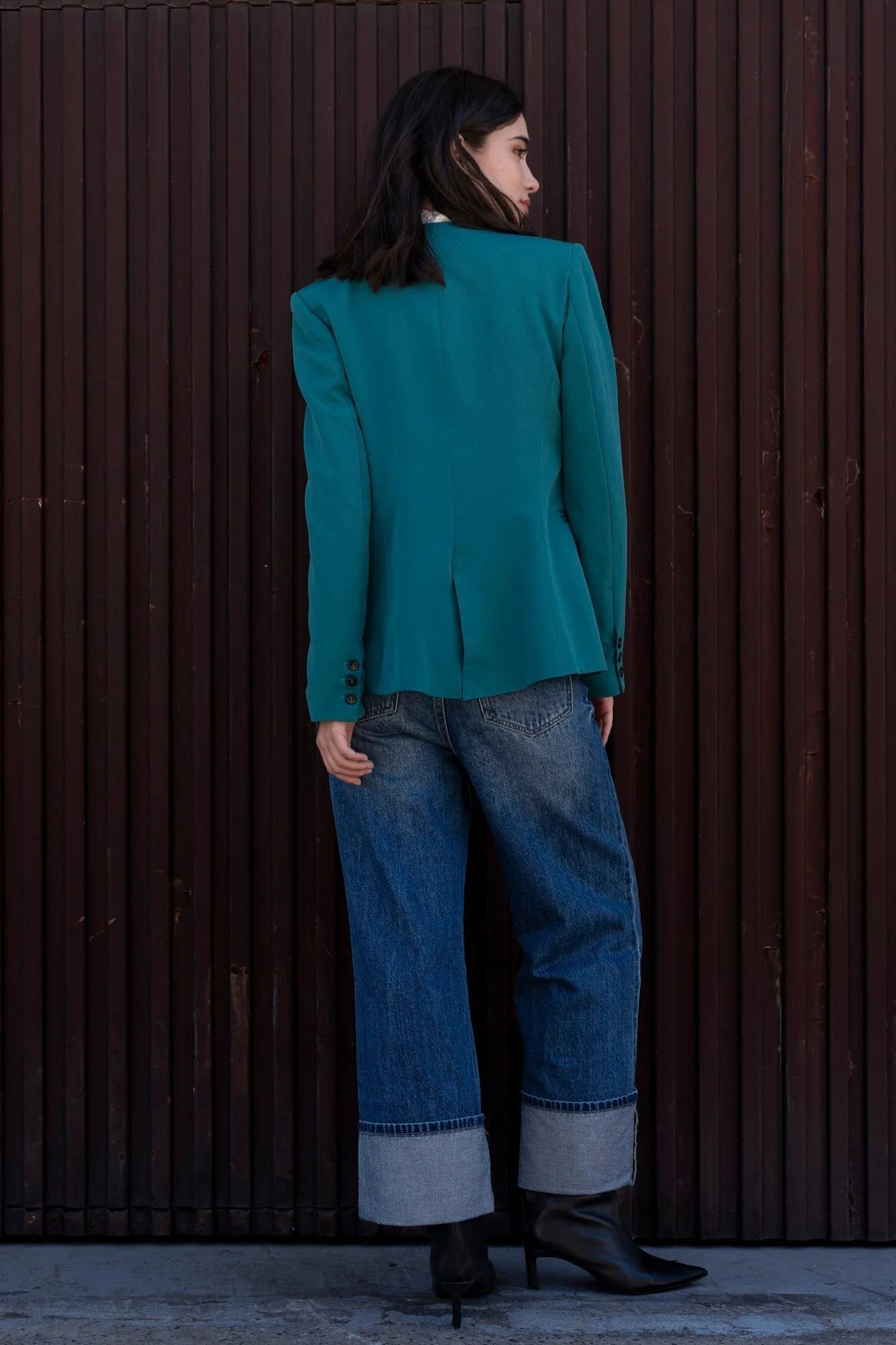 Vue arrière d'une femme dans un blazer vert femme, sans col, stylé avec un jean large, mettant en avant le design sophistiqué et contemporain.