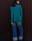 Vue arrière d'une femme dans un blazer vert femme, sans col, stylé avec un jean large, mettant en avant le design sophistiqué et contemporain.
