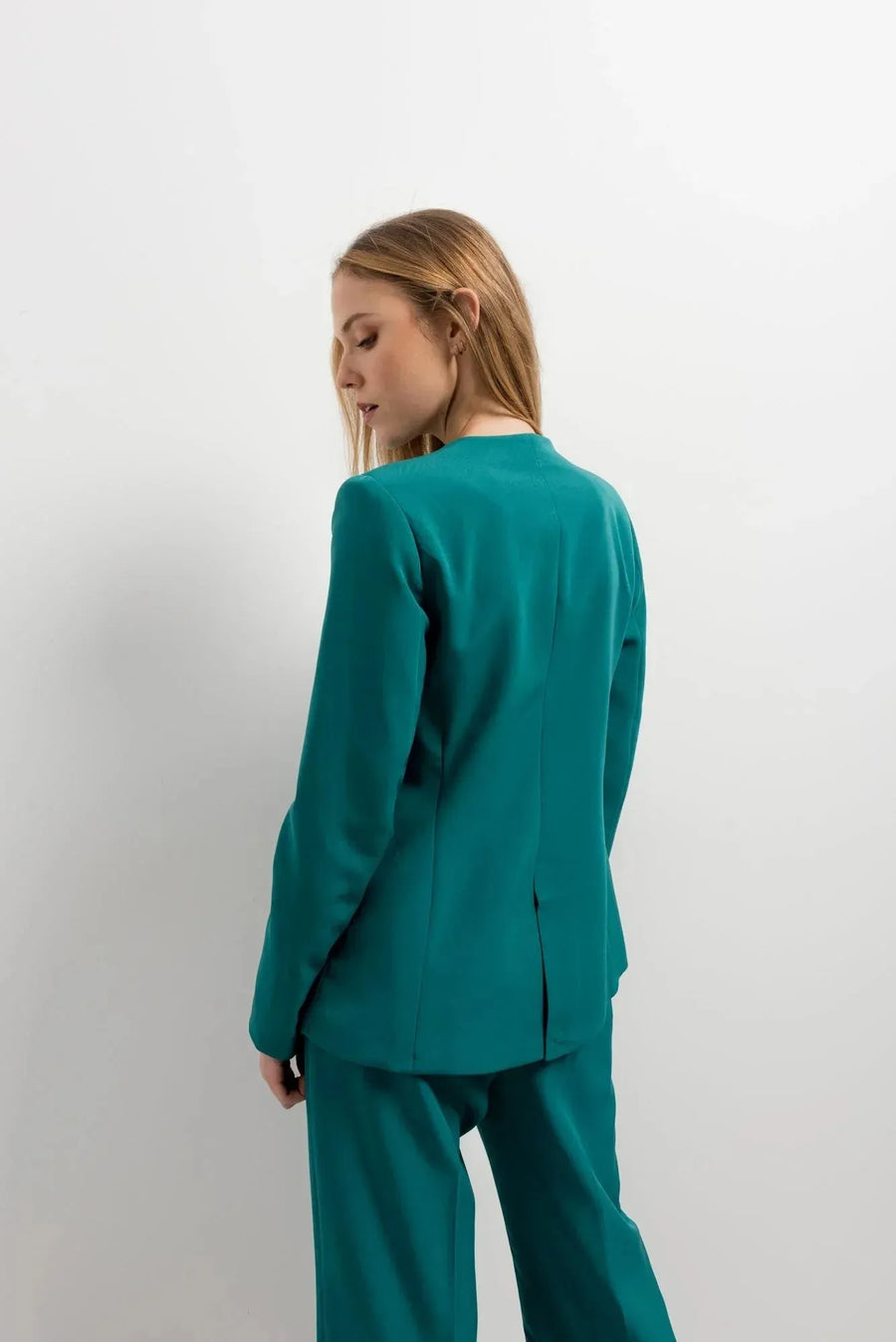 Femme vue de dos dans un blazer vert femme ajusté sans col, avec un pantalon coordonné, mettant en avant le confort et le style moderne.