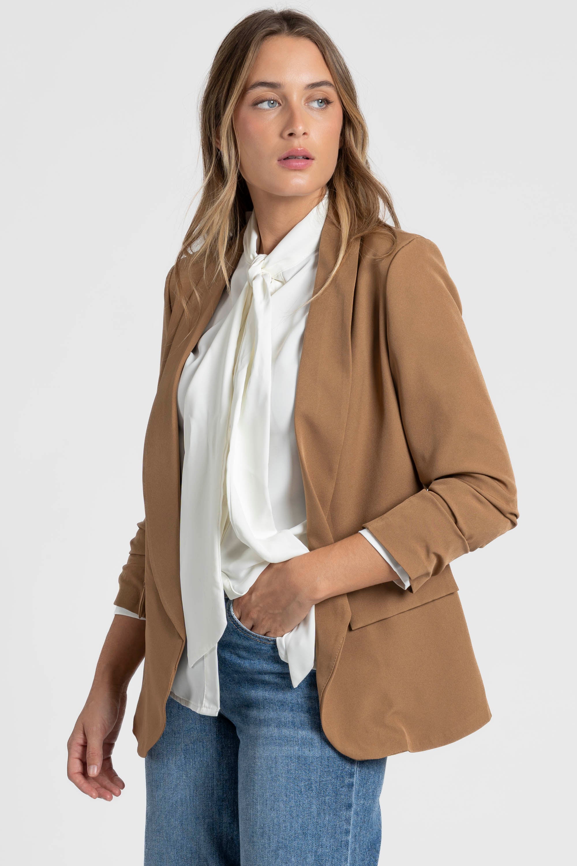 Femme portant un blazer femme chic crème, cascade de vêtements en arrière-plan pour un look branché.