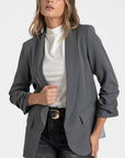 Zoom sur un blazer femme chic gris avec manches froncées, présenté sur un modèle avec un haut blanc.