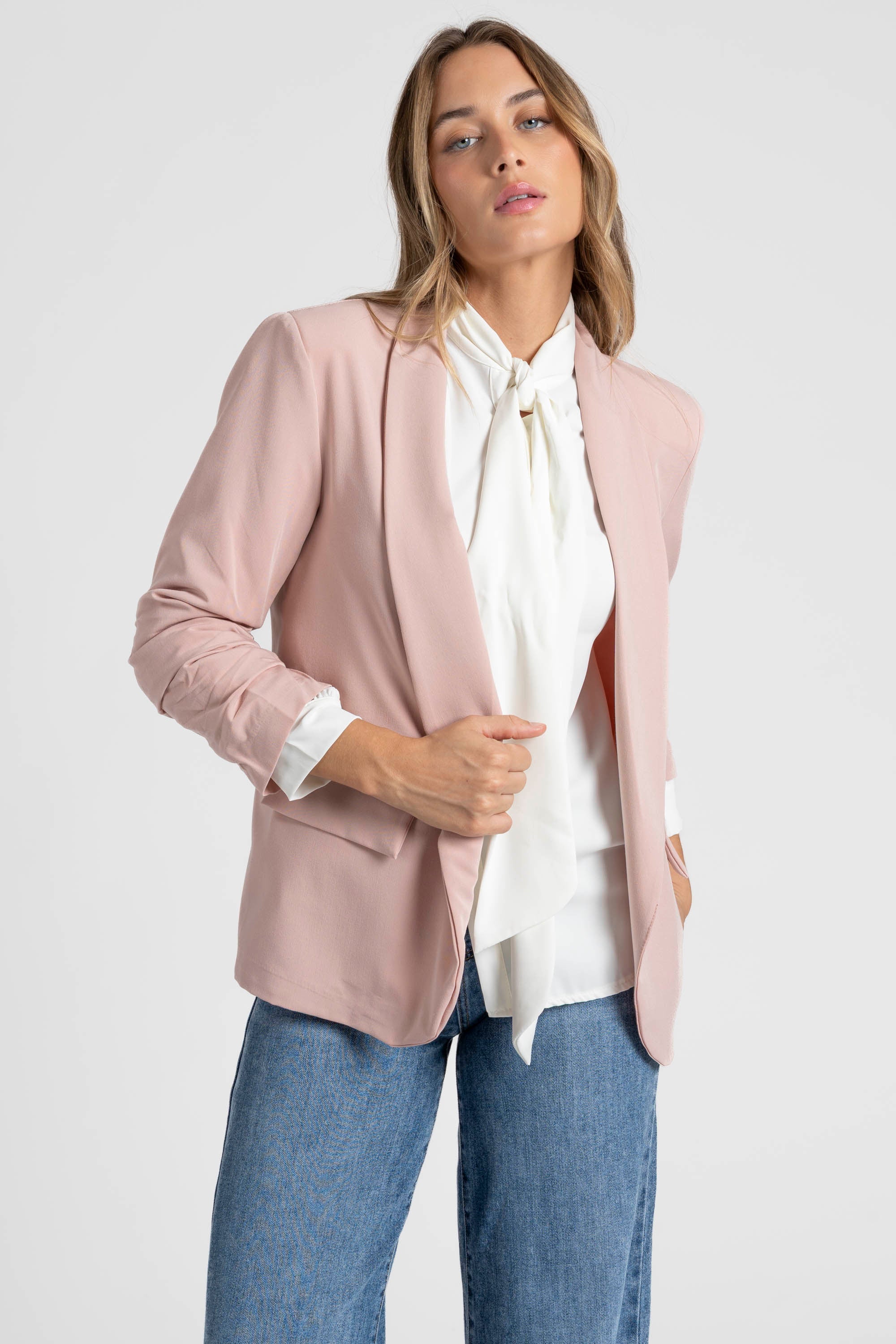 Femme dans un blazer femme chic rose poudré, associée à une chemise blanche pour un look raffiné.