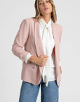 Femme dans un blazer femme chic rose poudré, associée à une chemise blanche pour un look raffiné.