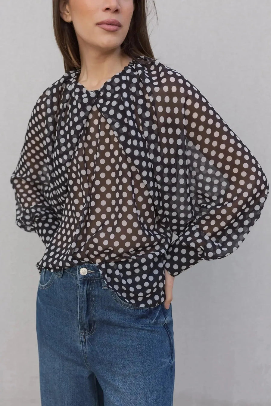 Vue rapprochée d'une femme en chemisier à pois noire transparente, mettant en valeur le motif et le style chic, une pièce tendance pour toutes occasions. Chemisier à pois femme.