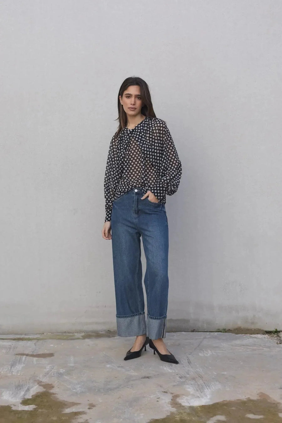 Femme en chemisier à pois noire transparente, posé avec confiance en jean, idéale pour le bureau ou une sortie entre amis. Chemisier à pois femme.