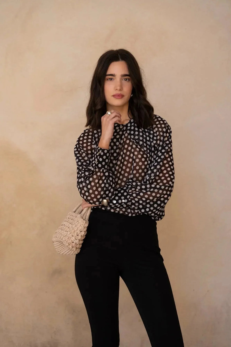 Gros plan sur une femme en chemisier à pois noire transparente, exhibant une allure élégante avec cheveux détachés et un petit sac, parfait pour un look moderne. Chemisier à pois femme.