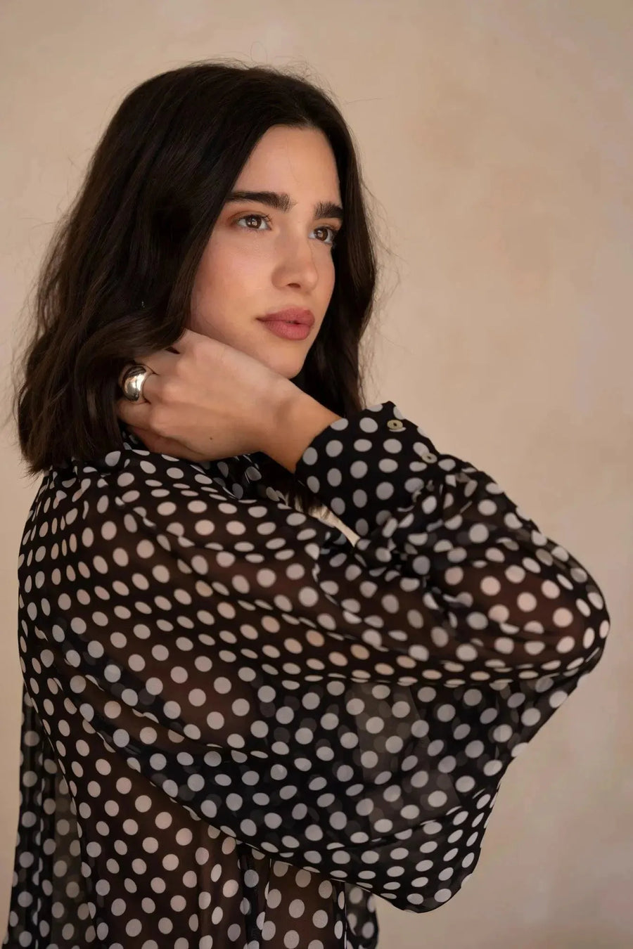 Femme en chemisier à pois noire transparent avec détails élégants, mettant en valeur un style sûr de soi, idéal pour ajouter une touche de mode à sa garde-robe. Chemisier à pois femme.