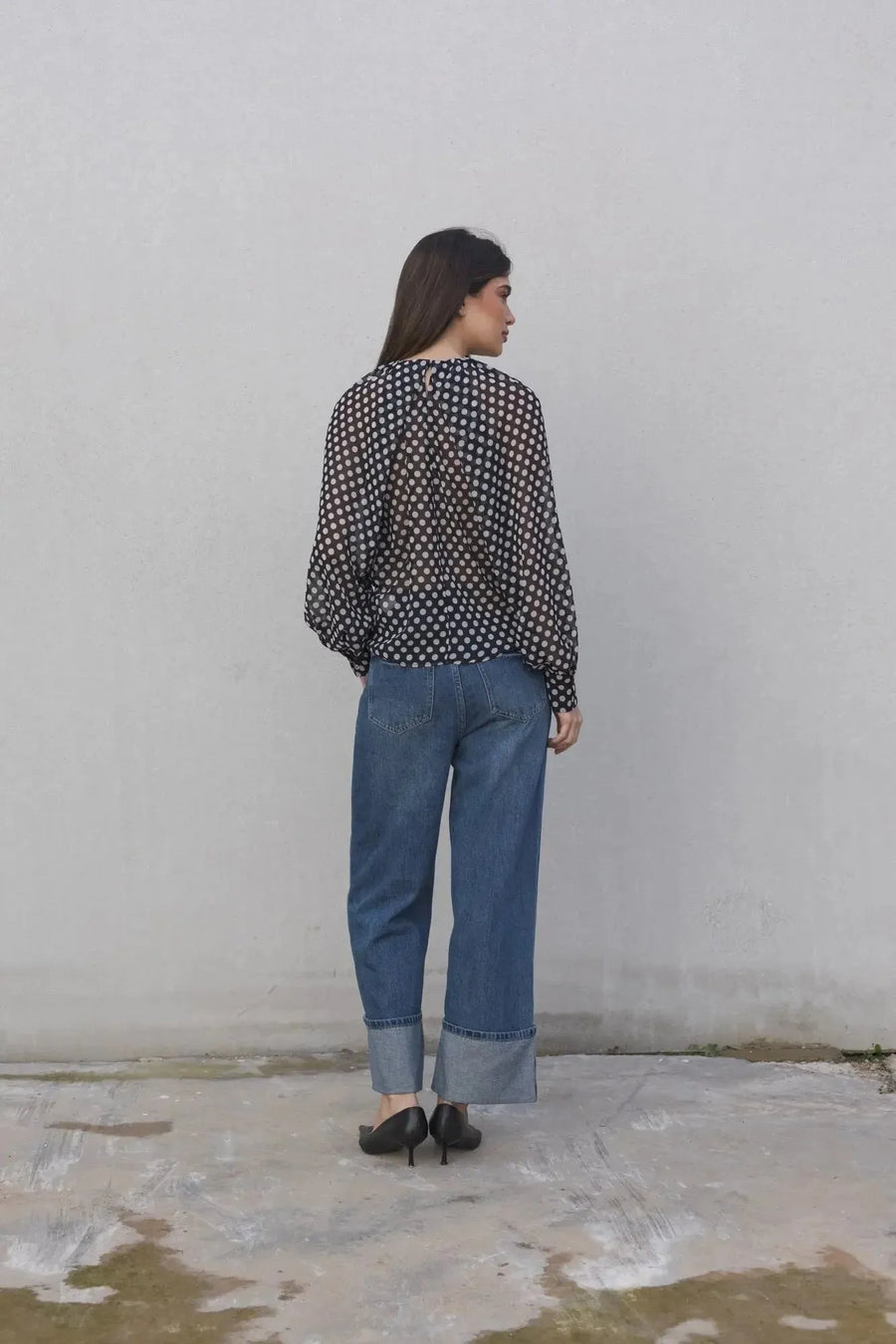 Femme vue de dos, arborant un chemisier à pois noire transparente, associé à un jean pour un look élégant et casual en toute simplicité. Chemisier à pois femme.