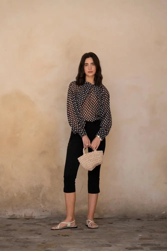 Femme portant une blouse à pois noire transparente, pantalon capri noir et sandales plates