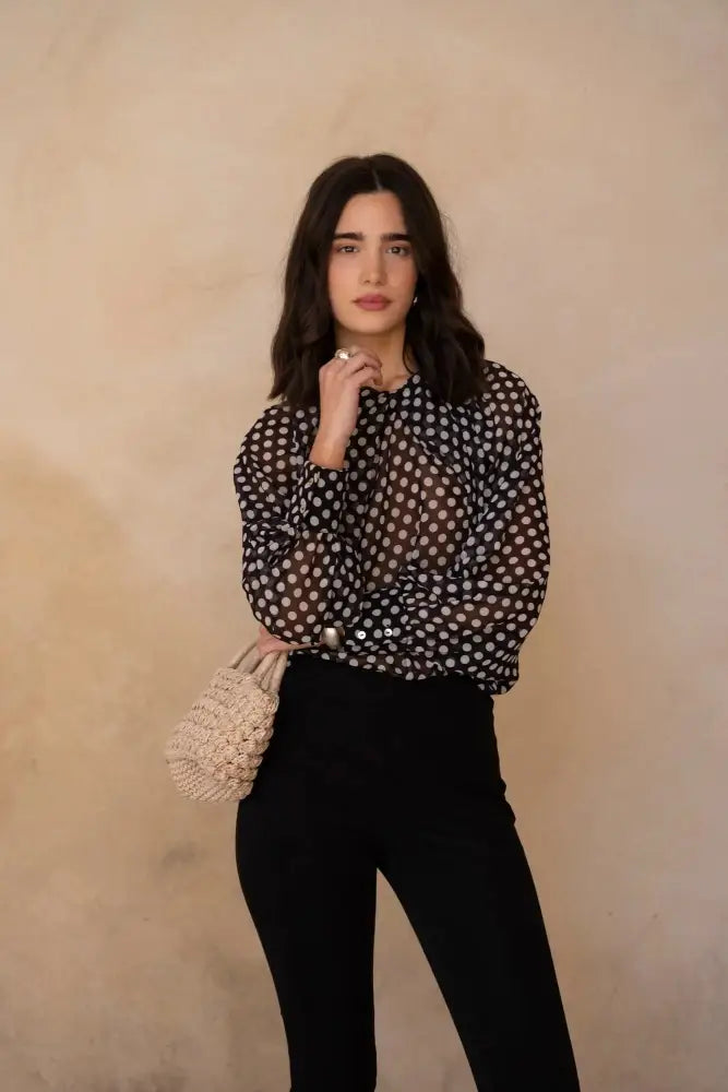 Femme portant une blouse à pois noire transparente et un sac en osier beige