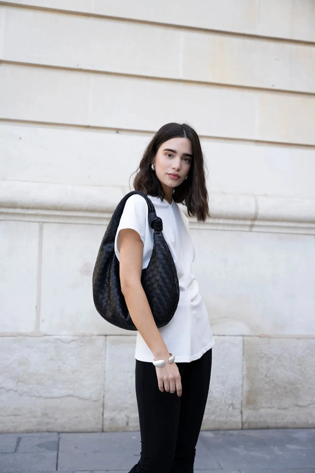 Femme portant une blouse blanche élégante col V minimaliste, avec un sac noir, dans un cadre urbain. Idéal pour un look chic et décontracté, mettant en avant la blouse blanche femme.